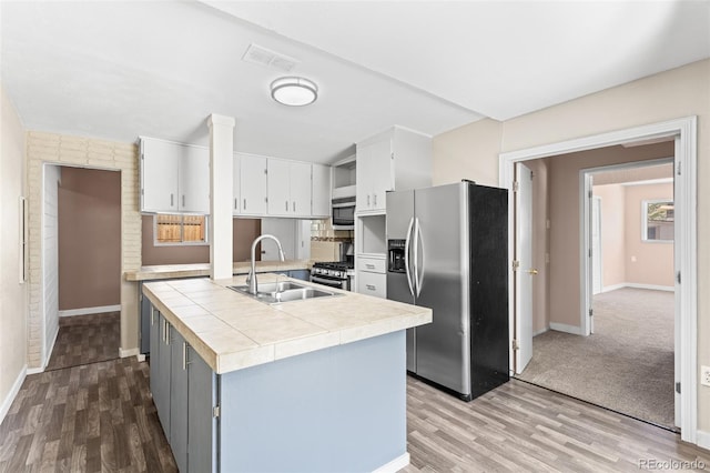 kitchen with a kitchen island with sink, stainless steel appliances, sink, light wood-type flooring, and white cabinets