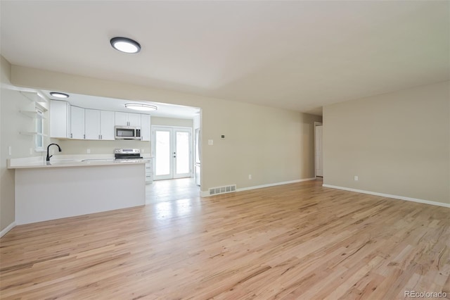 unfurnished living room with french doors, baseboards, light wood finished floors, and visible vents