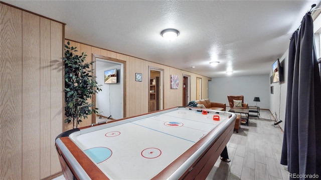 playroom with light hardwood / wood-style flooring, a textured ceiling, and wood walls