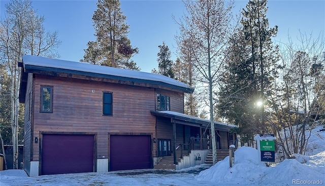 snow covered property featuring a porch and a garage