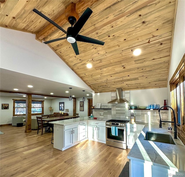 kitchen with white cabinets, wall chimney range hood, sink, stainless steel gas stove, and decorative light fixtures