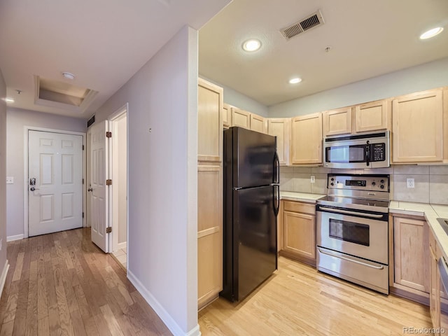 kitchen featuring appliances with stainless steel finishes, backsplash, light hardwood / wood-style floors, and light brown cabinets