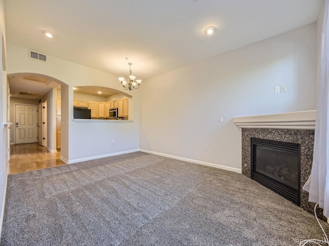 unfurnished living room featuring a high end fireplace, carpet floors, and an inviting chandelier