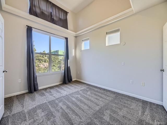 unfurnished room featuring a wealth of natural light, a towering ceiling, and dark colored carpet