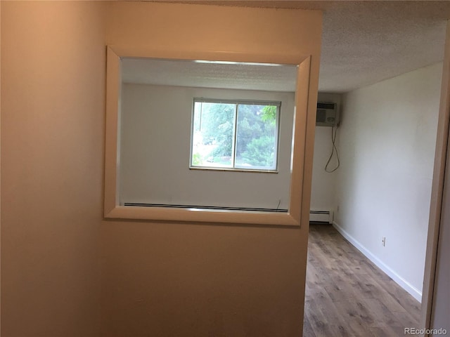 interior space featuring a wall mounted air conditioner, a textured ceiling, wood finished floors, baseboards, and baseboard heating