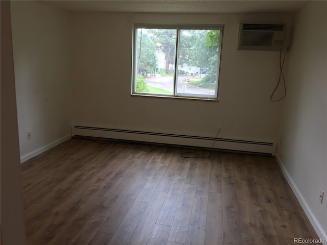 unfurnished room featuring a wall mounted air conditioner, wood finished floors, baseboards, and baseboard heating