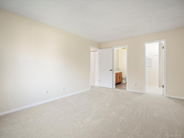 unfurnished bedroom with a closet, ensuite bathroom, light carpet, a textured ceiling, and baseboards