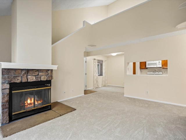 unfurnished living room with baseboards, carpet, a fireplace, high vaulted ceiling, and a sink