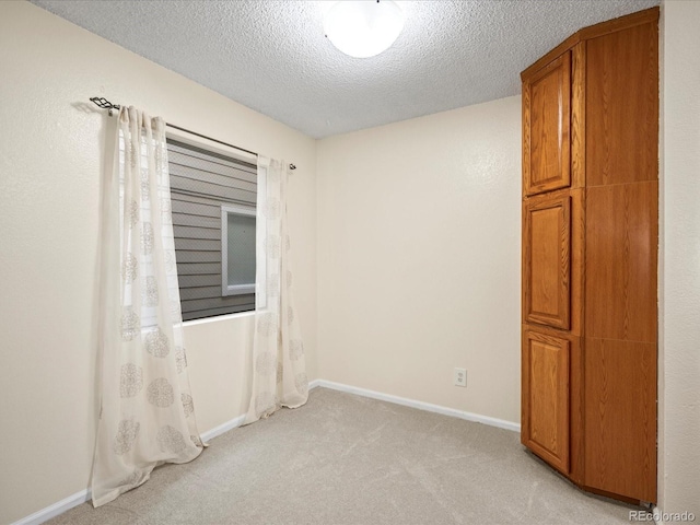 empty room featuring light colored carpet, a textured ceiling, and baseboards