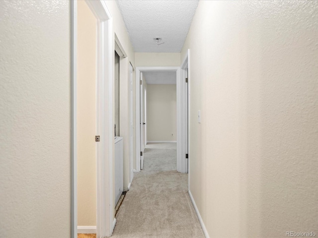 hallway with light carpet, baseboards, a textured ceiling, and a textured wall