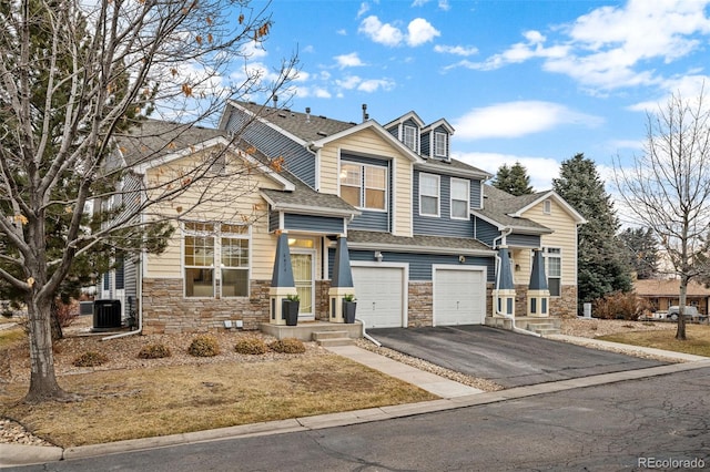 view of front of property with a shingled roof, central AC, a garage, stone siding, and driveway