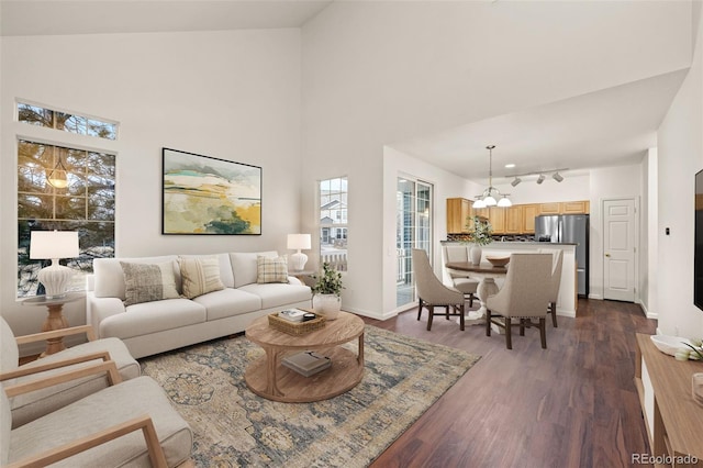 living room featuring a high ceiling, an inviting chandelier, dark wood-type flooring, track lighting, and baseboards