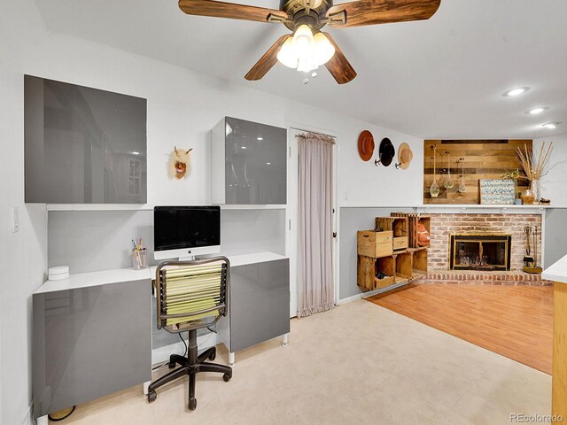 office with ceiling fan, light hardwood / wood-style floors, and a brick fireplace