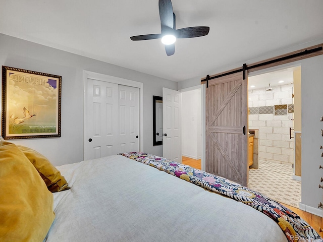 bedroom featuring ensuite bath, ceiling fan, a barn door, hardwood / wood-style floors, and a closet