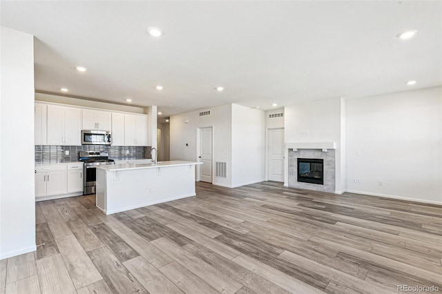 kitchen featuring backsplash, open floor plan, stainless steel appliances, white cabinetry, and a kitchen island with sink