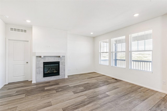 unfurnished living room featuring wood finished floors, visible vents, baseboards, recessed lighting, and a tiled fireplace