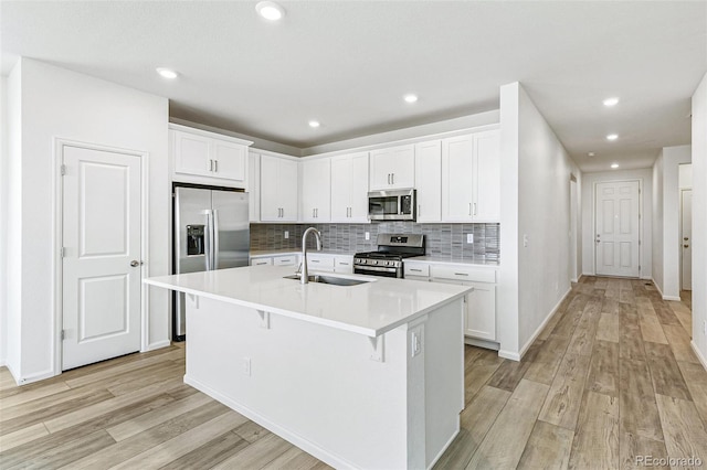 kitchen with light wood-type flooring, a kitchen island with sink, a sink, stainless steel appliances, and light countertops