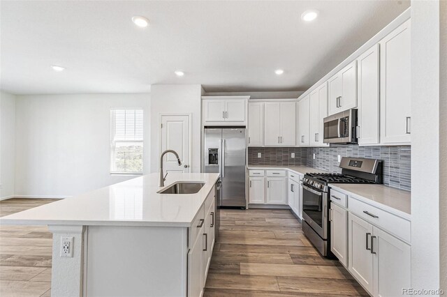 kitchen with light wood-style flooring, a center island with sink, a sink, tasteful backsplash, and appliances with stainless steel finishes