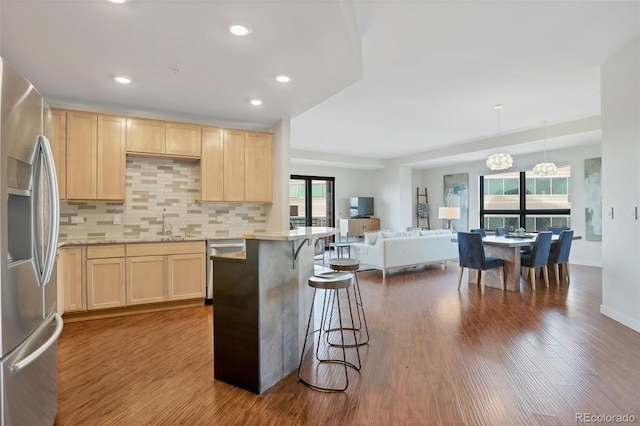 kitchen featuring decorative light fixtures, a kitchen bar, light brown cabinetry, and stainless steel fridge