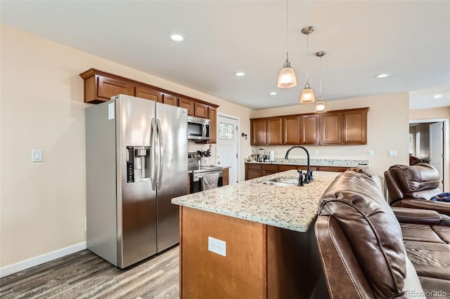 kitchen with open floor plan, light wood-style flooring, light stone countertops, appliances with stainless steel finishes, and a sink