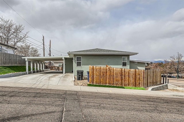 view of front facade featuring concrete driveway, stucco siding, fence, and an attached carport