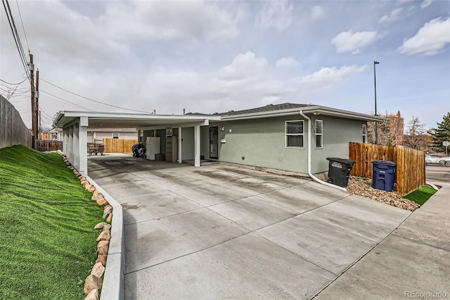 view of front of home featuring a front yard, a carport, fence, stucco siding, and driveway