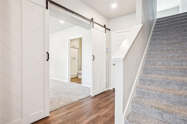 stairs with a barn door, wood finished floors, and baseboards