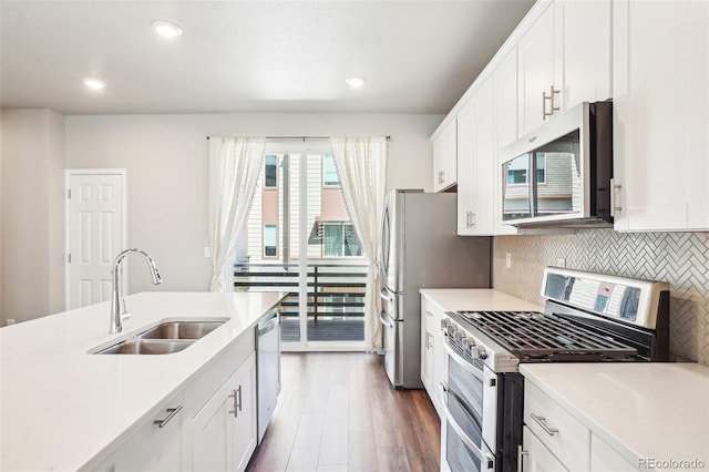 kitchen featuring stainless steel appliances, a sink, backsplash, wood finished floors, and white cabinets