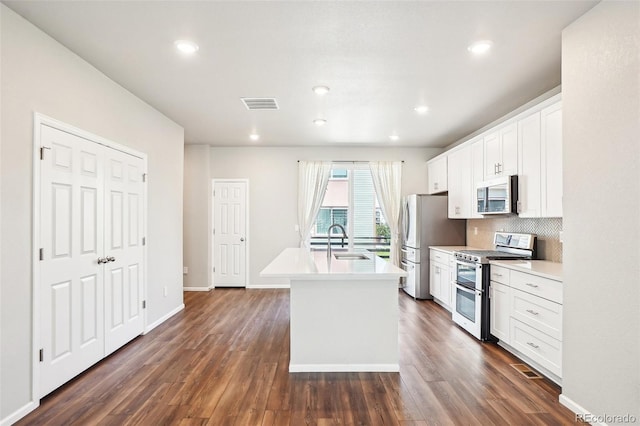 kitchen featuring stainless steel appliances, a sink, a center island with sink, backsplash, and white cabinetry