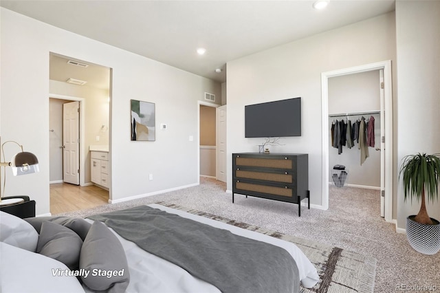 bedroom featuring a spacious closet, ensuite bath, light colored carpet, baseboards, and recessed lighting