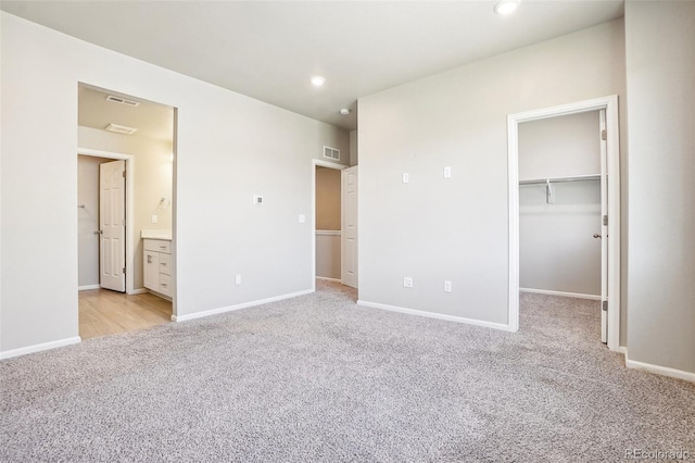 unfurnished bedroom featuring light carpet, a walk in closet, recessed lighting, baseboards, and connected bathroom
