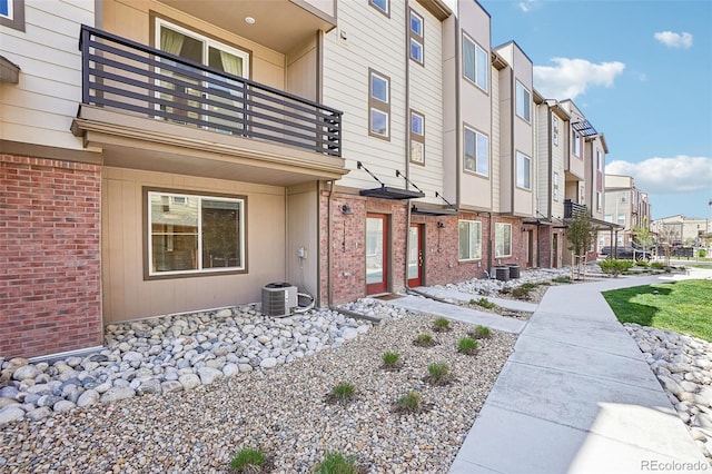 entrance to property featuring a balcony, a residential view, brick siding, and cooling unit