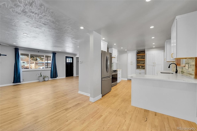 kitchen with sink, light hardwood / wood-style flooring, appliances with stainless steel finishes, white cabinets, and kitchen peninsula