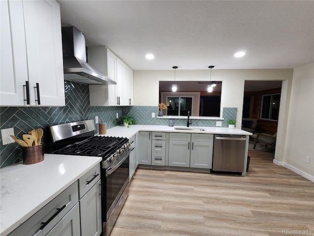 kitchen with hanging light fixtures, stainless steel appliances, wall chimney range hood, gray cabinetry, and sink