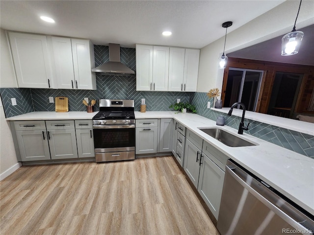 kitchen featuring sink, wall chimney exhaust hood, pendant lighting, gray cabinetry, and appliances with stainless steel finishes