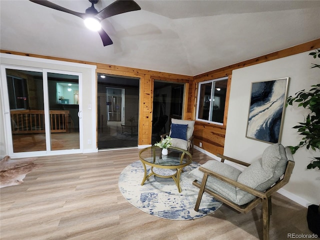 living area with ceiling fan, light hardwood / wood-style floors, wooden walls, and lofted ceiling