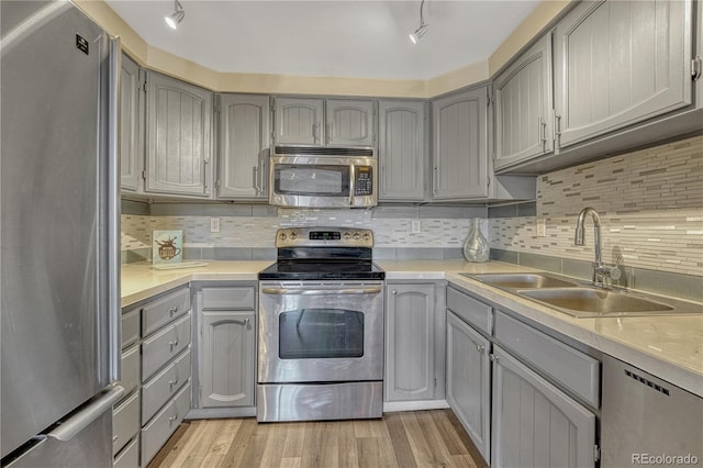 kitchen featuring light wood-style flooring, gray cabinets, a sink, appliances with stainless steel finishes, and decorative backsplash