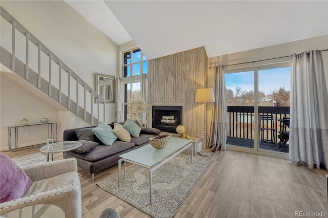 living area with stairway, high vaulted ceiling, a large fireplace, and wood finished floors