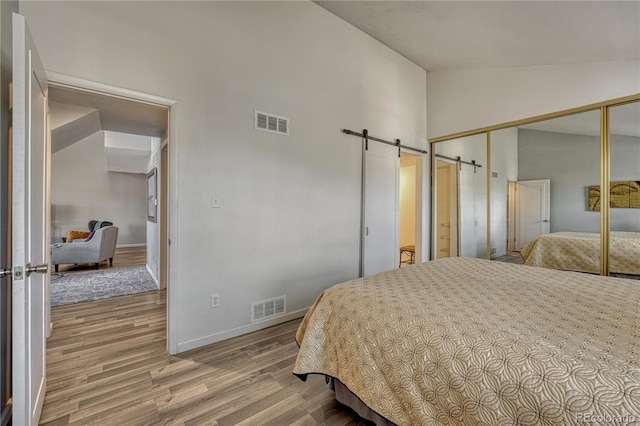 bedroom with a barn door, visible vents, a closet, and light wood finished floors