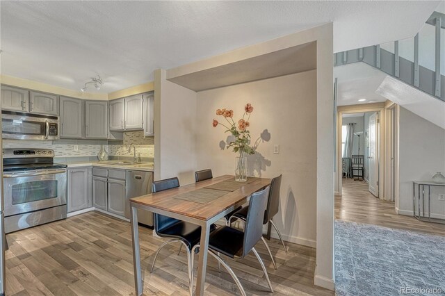 kitchen with backsplash, gray cabinetry, wood finished floors, stainless steel appliances, and a sink