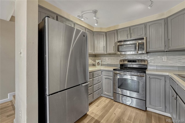 kitchen featuring backsplash, gray cabinets, appliances with stainless steel finishes, and light wood-style flooring