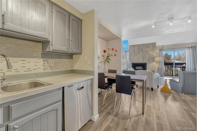 kitchen featuring light wood finished floors, gray cabinets, a sink, backsplash, and light countertops