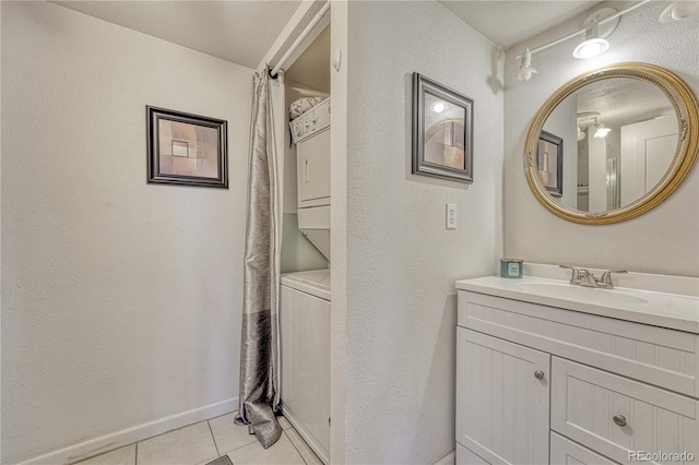 full bath with vanity, baseboards, tile patterned flooring, stacked washer and dryer, and a textured wall