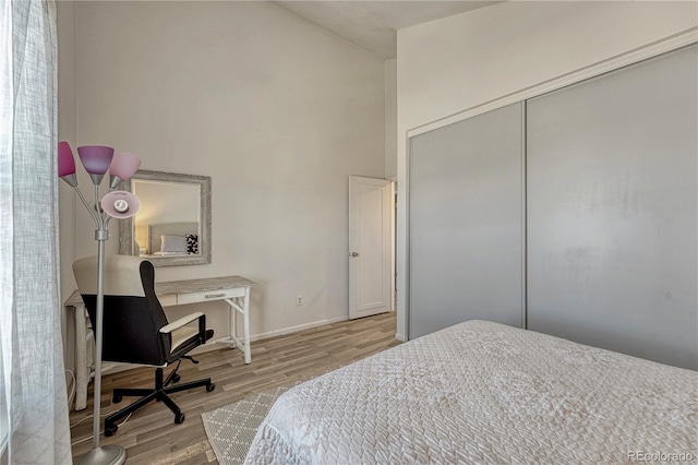 bedroom featuring a closet, baseboards, wood finished floors, and a towering ceiling