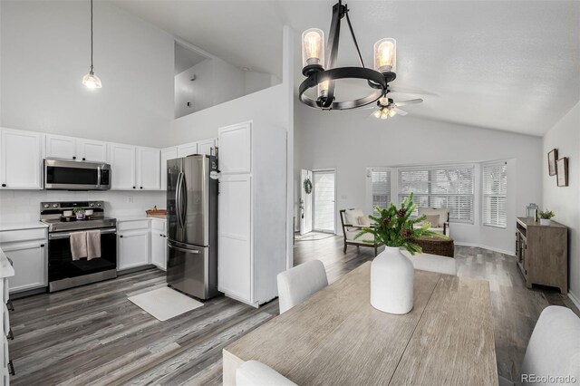 dining space with lofted ceiling, ceiling fan with notable chandelier, dark wood-type flooring, and a textured ceiling