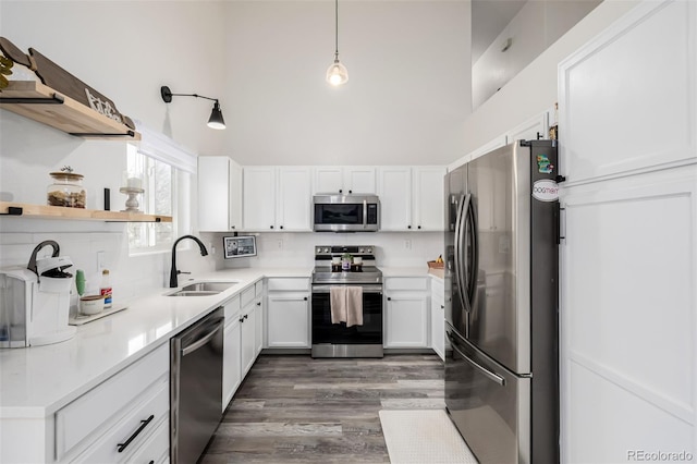 kitchen with pendant lighting, sink, a towering ceiling, stainless steel appliances, and white cabinets