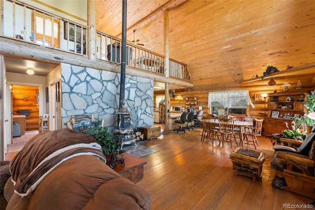 living room with high vaulted ceiling, hardwood / wood-style floors, rustic walls, wooden ceiling, and a wood stove