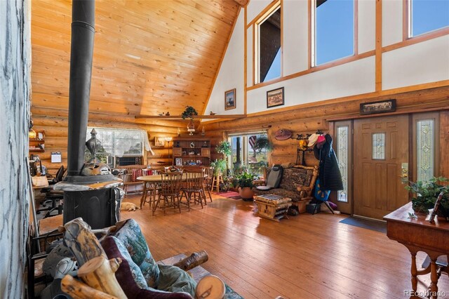 living room featuring a wood stove, rustic walls, hardwood / wood-style floors, and high vaulted ceiling