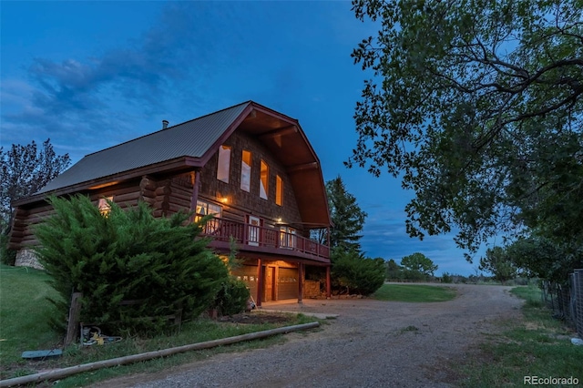 view of front of home with dirt driveway, log exterior, a wooden deck, metal roof, and an attached garage