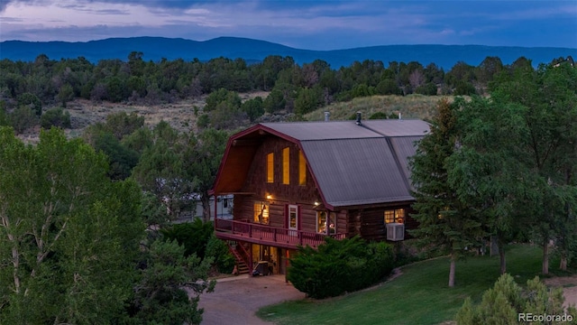 rear view of property featuring a gambrel roof, concrete driveway, log exterior, a view of trees, and metal roof